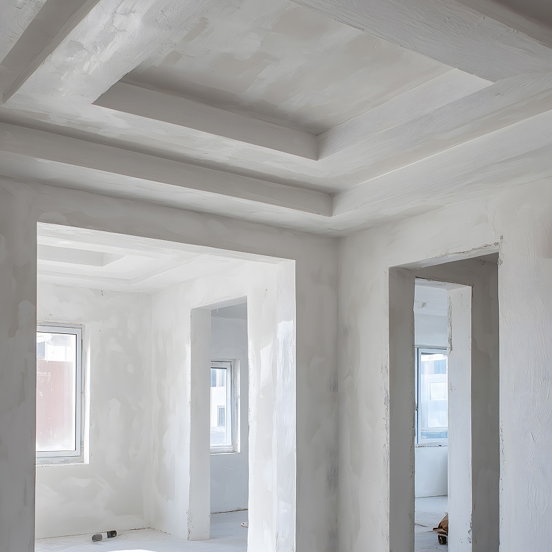 Intérieur d'un appartement en travaux, murs et plafond en plâtre brut avec coffrage rectangulaire et passages ouverts.
